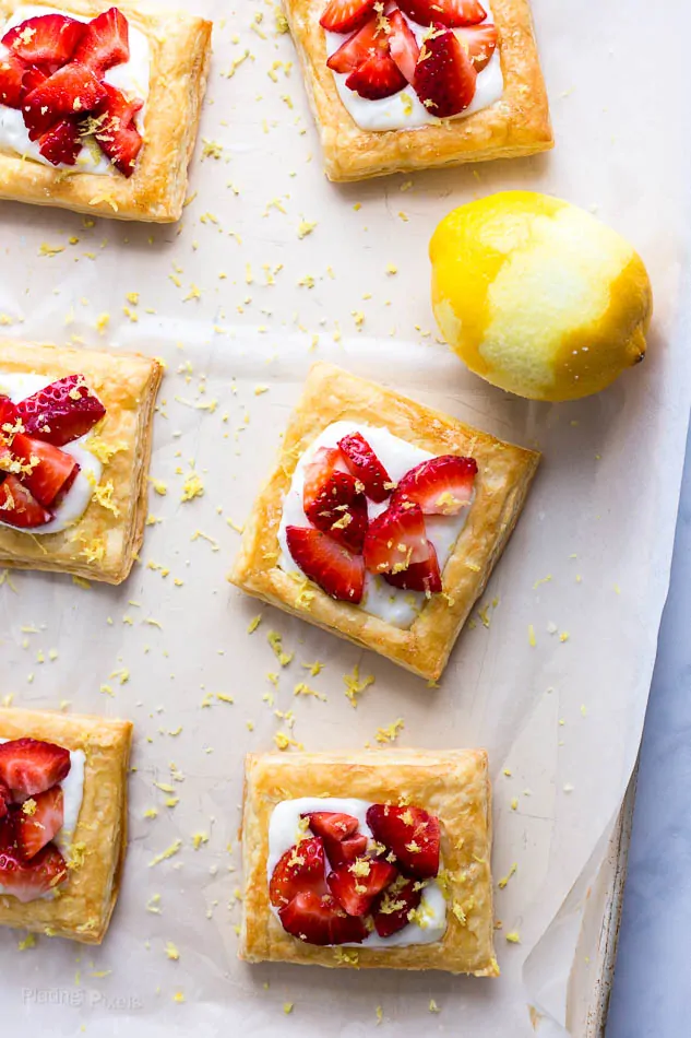 Six Strawberry Lemon Cream Breakfast Tarts on a baking sheet with halfway zested lemon