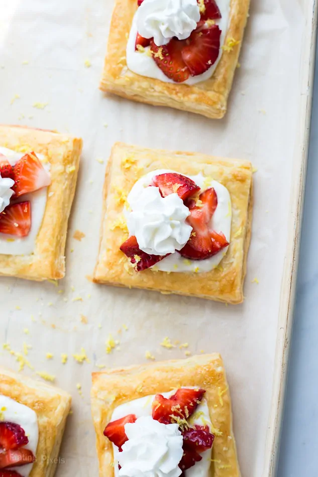 Five Strawberry Lemon Cream Breakfast Tarts on parchment paper with sprinkles of lemon zest