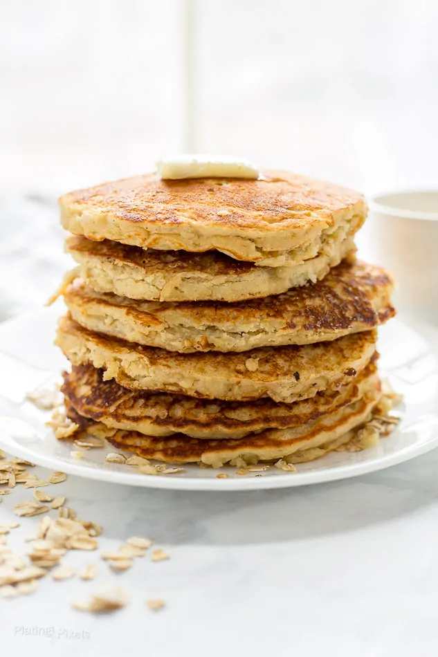 A close up of a stack of healthy Banana Oatmeal Pancakes on a plate next to window