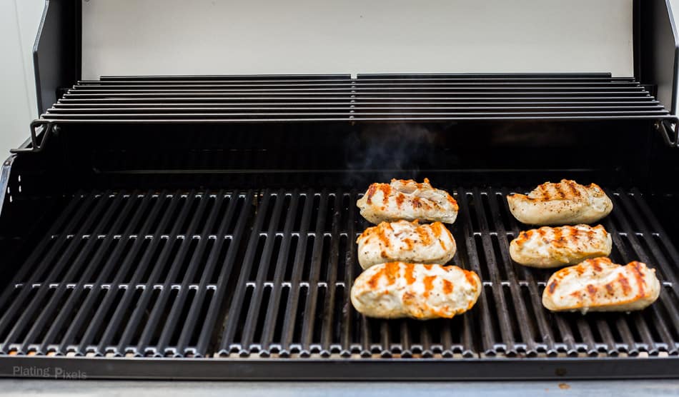 SIx grilled chicken breasts cooking on a gas grill