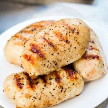 Moist Grilled Chicken Breasts on plate next to gas grill