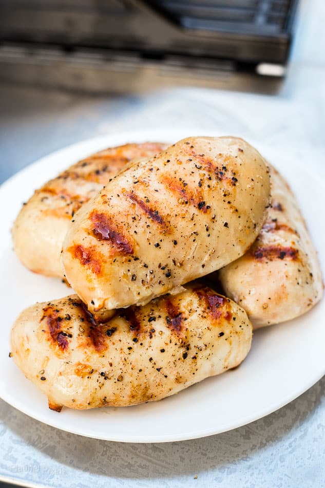 Perfectly cooked grilled chicken breasts with nice sear marks on plate next to gas grill