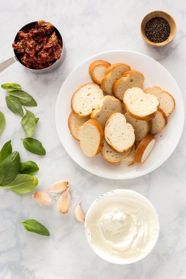 Ingredients for making sun-dried tomato ricotta crostini prepared on a marble surface