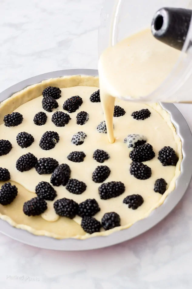 A process shot of pouring custard filling into a Blackberry Pie 