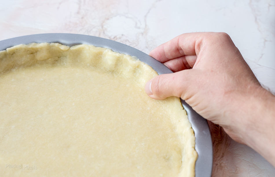 A process shot of pressing a pie crust into a pie dish 