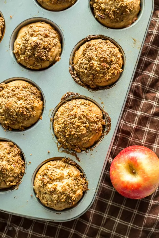 Lightened Up Apple Streusel Muffins in a muffin pan with an apple next to it 