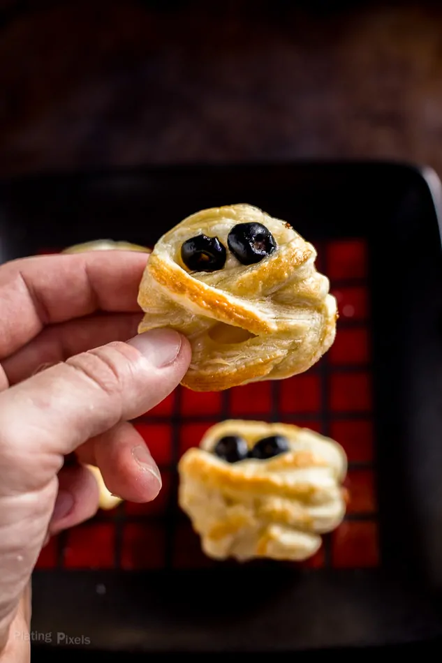 Hand holding just baked Halloween Puff Pastry Mummy Cheese Wheel