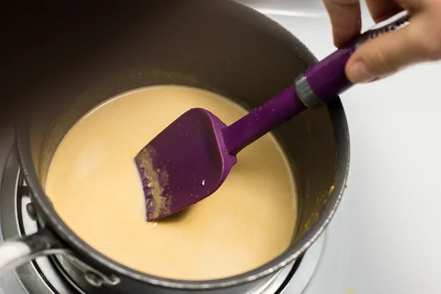 Stirring pumpkin spice milk mixture in saucepan on stove