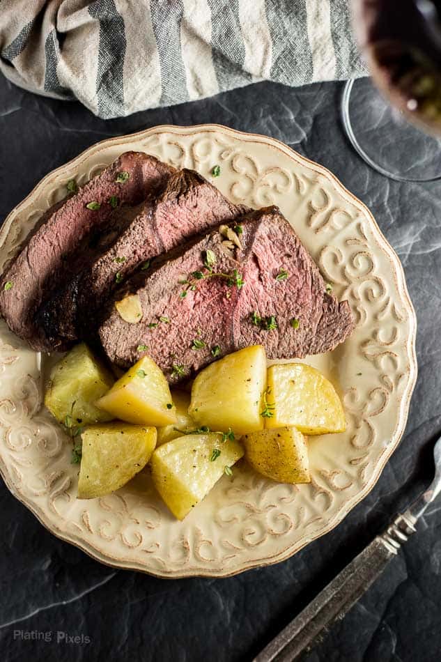 Sliced Red Wine Marinated Prime Rib with Potatoes on a plate next to glass of wine