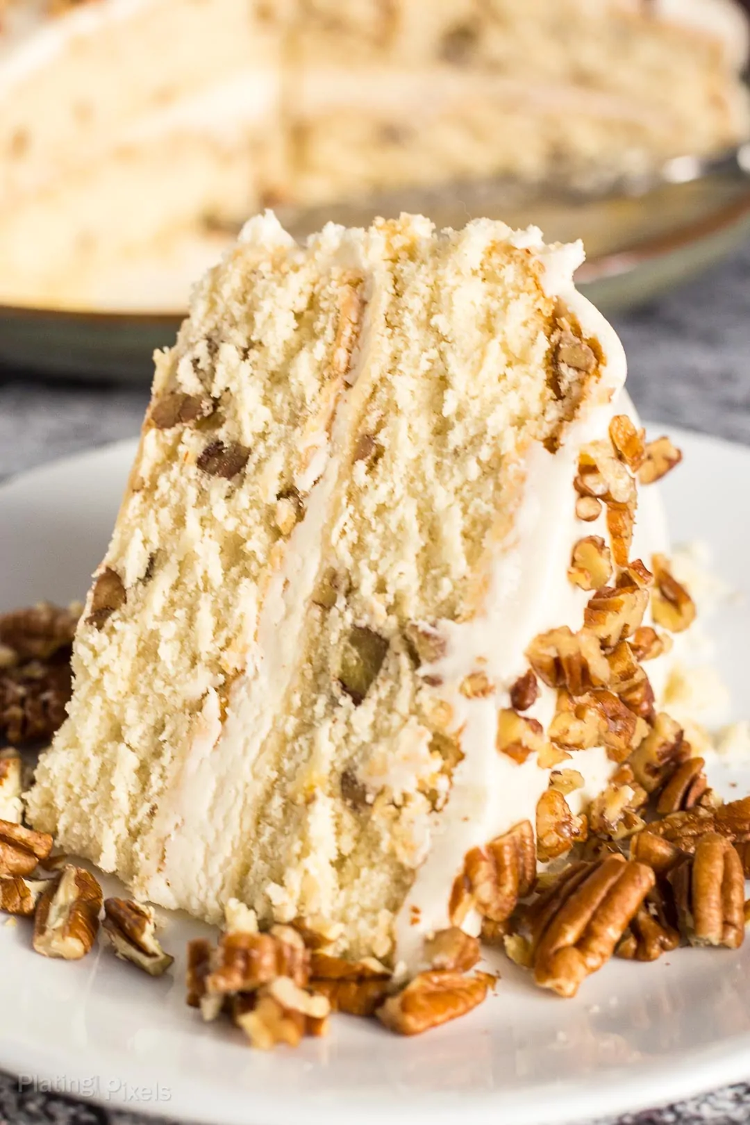 A close up of a slice of Butter Pecan Cake on a plate garnished with chopped pecans