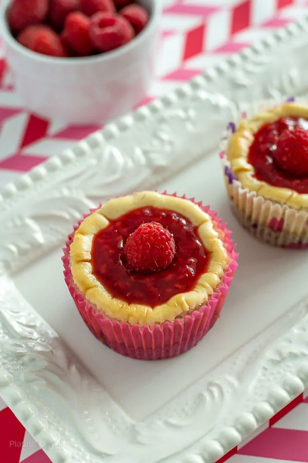 Mini Raspberry Cheesecake Muffins on a white plate with a bowl of raspberries in the background