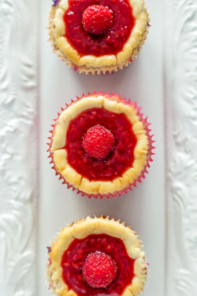 An overhead shot of three Raspberry Mini Cheesecake Muffins on a white plate