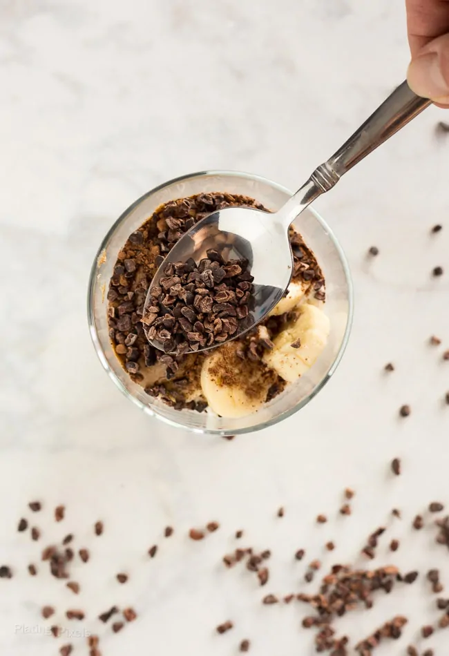 Spooning cocoa nibs to top off Chocolate Almond Butter Breakfast Parfaits