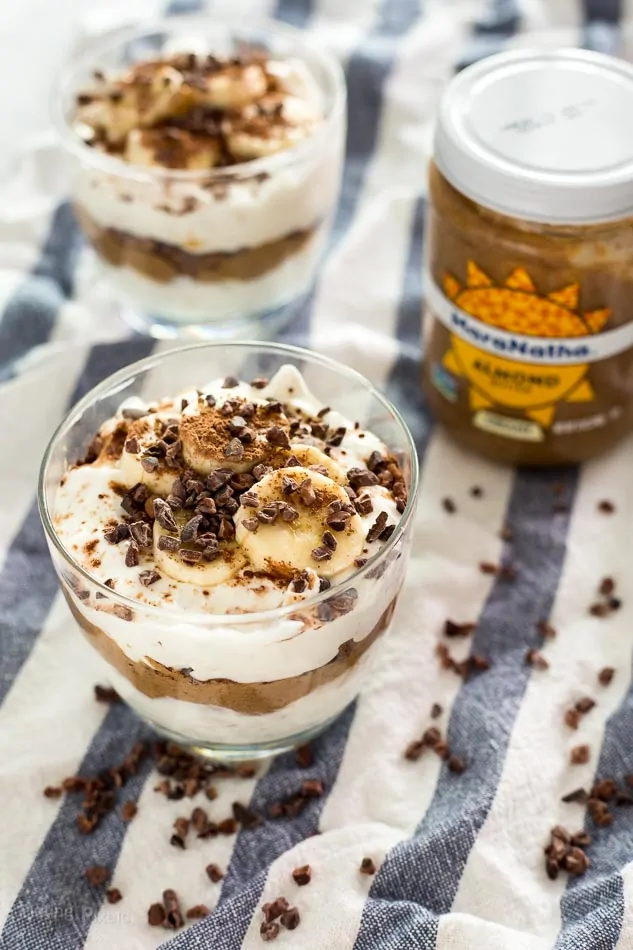 Two layered Chocolate Almond Butter Breakfast Parfaits in glasses next to a jar of almond butter