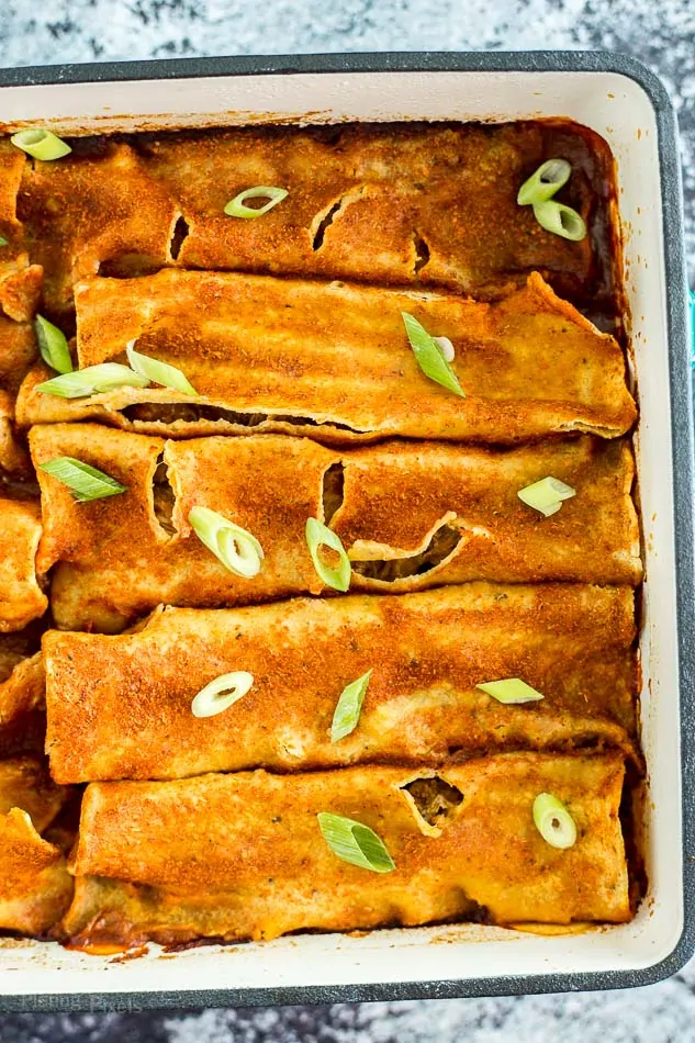 A close up of Slow Cooker Carnitas Enchiladas in a baking tray topped with green onions