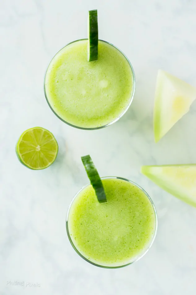 Two Cucumber Melon Cocktail Slushie in glass garnished with cucumber wedges