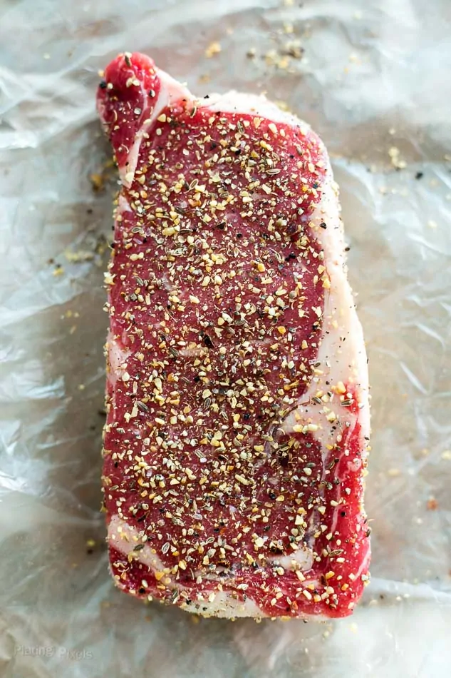 Process shot showing dry steak seasoning on a raw ribeye steak