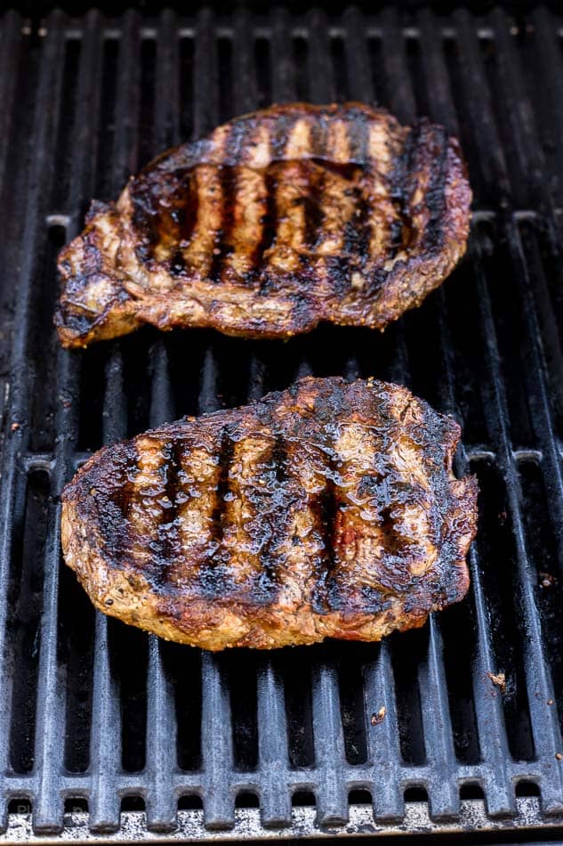 Two ribeye steaks grilling on a gas grill with nice sear marks