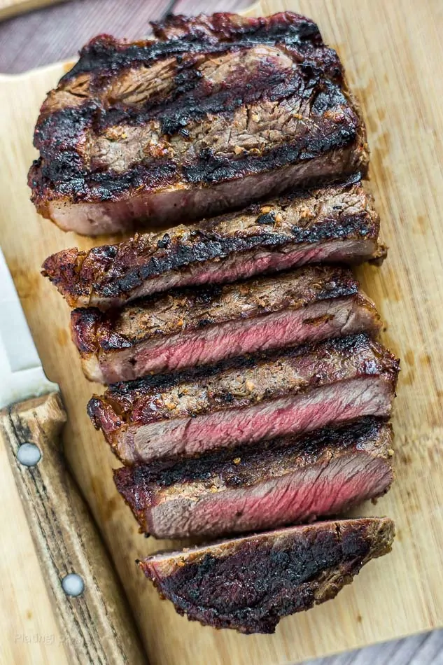 Grilled Ribeye Steak sliced and resting on a cutting board with knife next to it