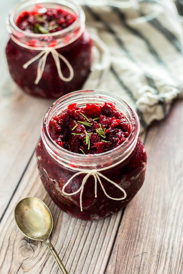 A close up of Homemade Cranberry Chutney in glass jars sitting on a wooden surface