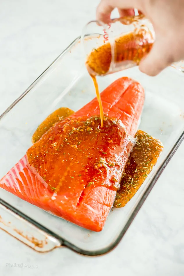 Process shot of drizzling maple glaze onto raw salmon fillet in a clear baking dish