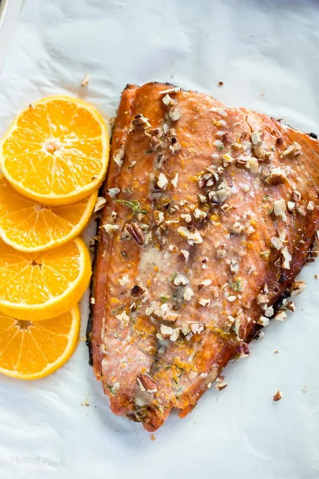 An overhead shot of just baked salmon with chopped pecans and slices of orange