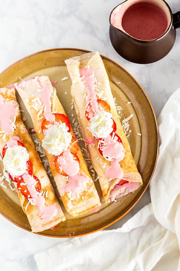 Three dairy-free crepes on a plate with a side of homemade strawberry coconut sauce