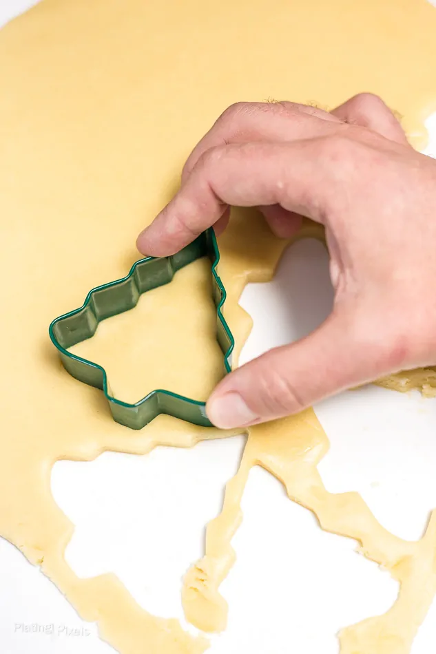 Cutting out sugar cookies with Christmas tree shaped cutter