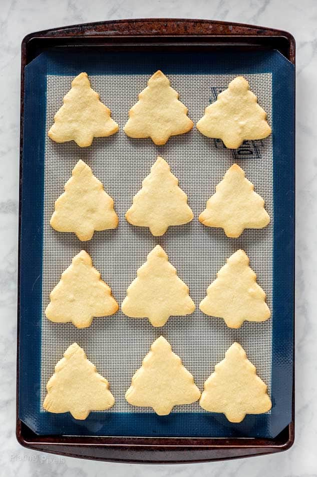 Twelve baked Christmas tree shaped sugar cookies on a baking sheet