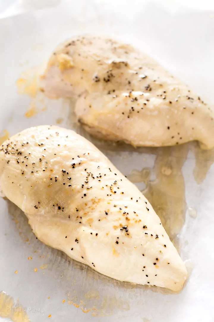 Two just baked chicken breasts over parchment paper in a baking dish