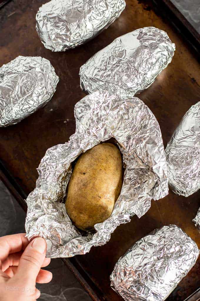 Hand unwrapping foil from a roasted potato on baking sheet