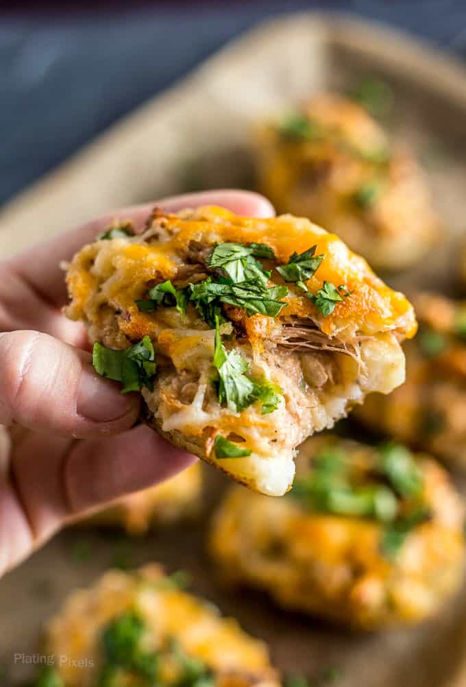 Hand holding Carnitas Loaded Potato Skins with bite taken out