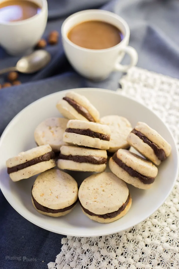 Pumpkin Spice Chocolate Shortbread Cookies sandwiches piled on a plate with coffee in background