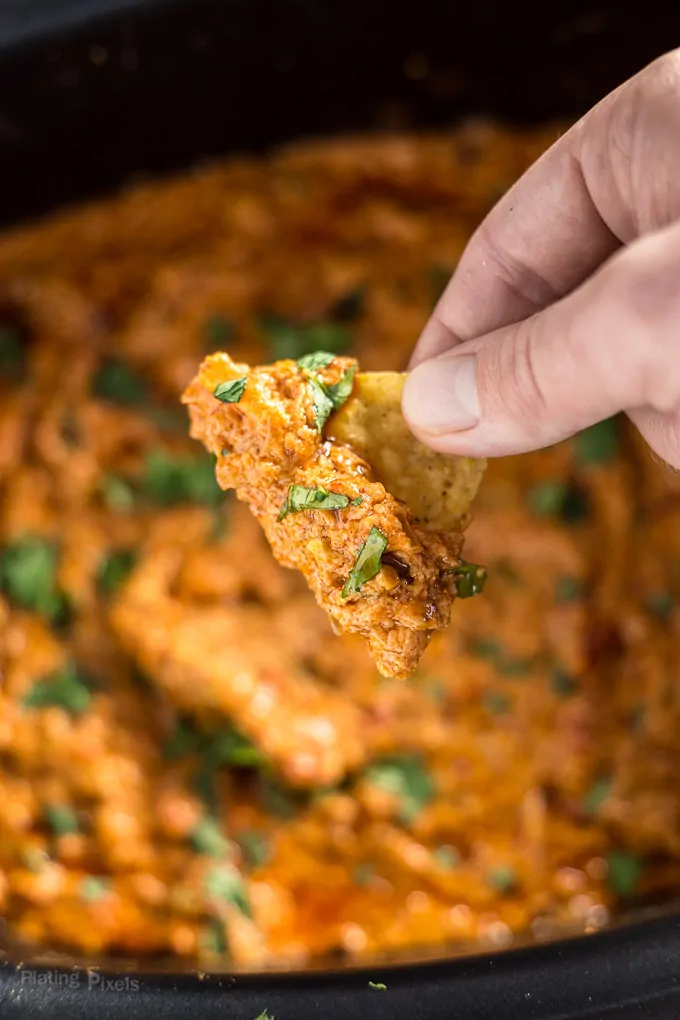 Dipping tortilla chip into pot of Slow Cooker Chorizo Queso Dip