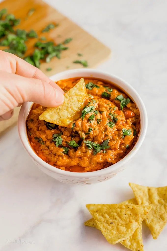 Hand dipping a tortilla chip into Slow Cooker Chorizo Queso Dip in a white bowl