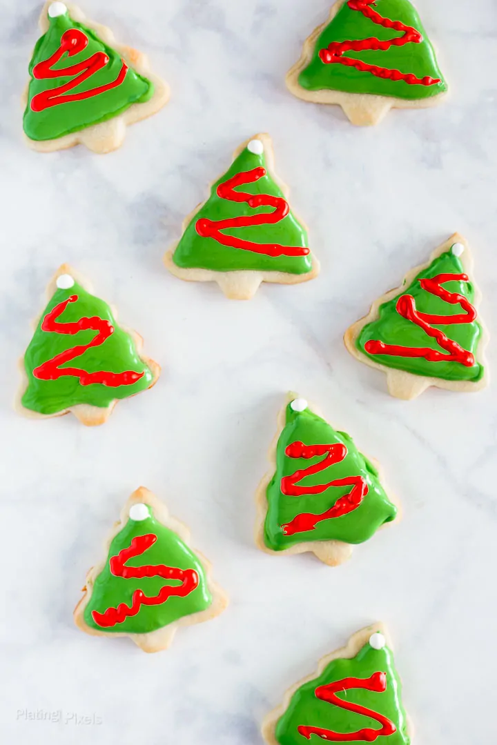 Overhead shot of decorated Christmas tree cookies with royal icing over marble background