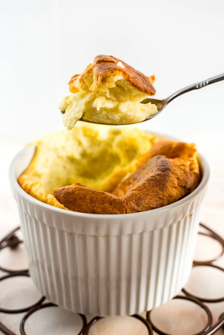 A scoop of Easy Cheese Souffle on a spoon hovering over ramekin of cheese souffle