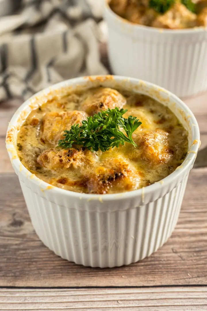 Angled shot of French Onion Soup in a ramekin on a wooden table