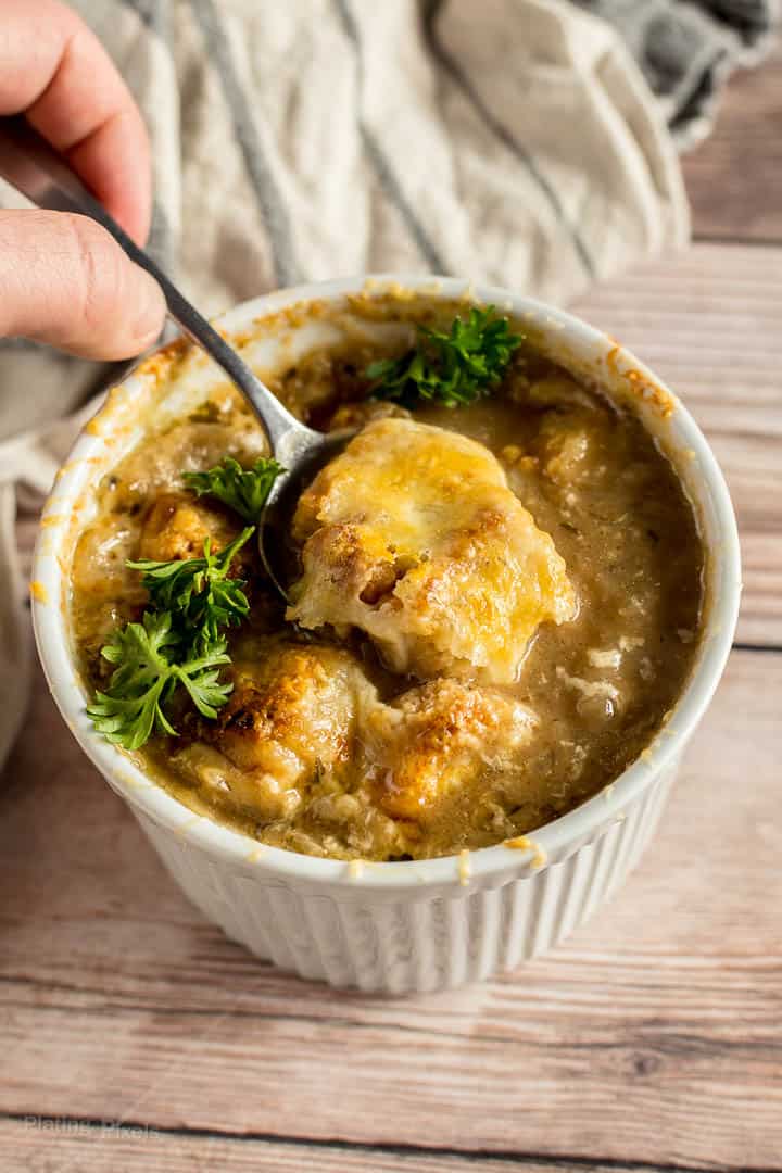 Hand scooping bite of prepared French Onion Soup from a ramekin