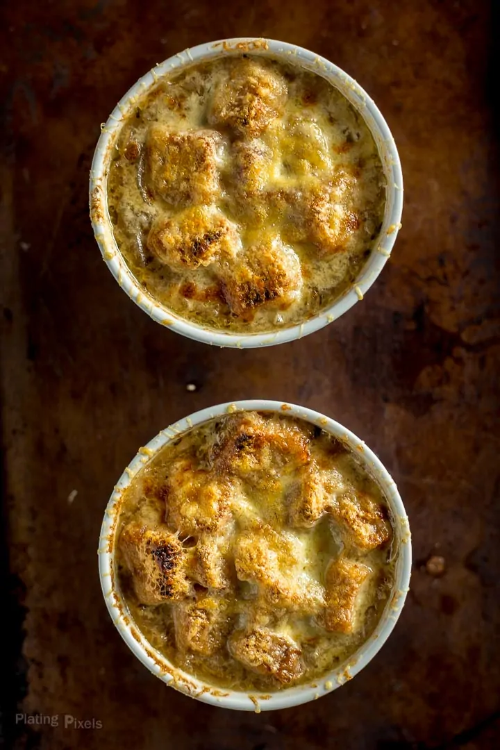 Overhead shot of two ramekins of French Onion Soup just broiled on a baking sheet