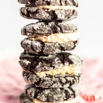 Four prepared Peppermint Buttercream Chocolate Crackle Cookie Sandwiches stacked over Christmas themed linens