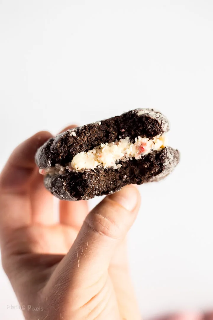 Hand holding a Peppermint Buttercream Chocolate Crackle Cookie Sandwiches with bite taken out of it