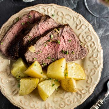 Slices of Red Wine Marinated Prime Rib next to cooked potatoes