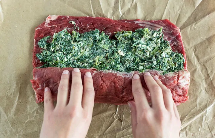 Overhead shot of hands rolling creamy spinach filing inside of flattened flank steak