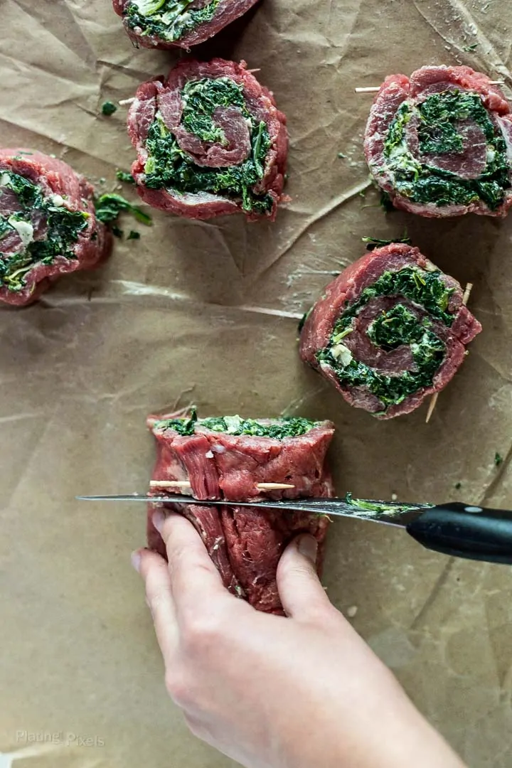 Hand slicing rolled Creamy Spinach Stuffed Flank Steak Pinwheels with a knife