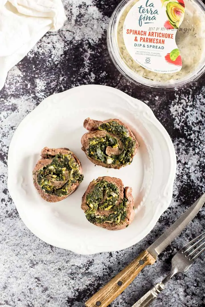 Three Creamy Spinach Stuffed Flank Steak Pinwheels on a plate next to container of La Terra Fina dip