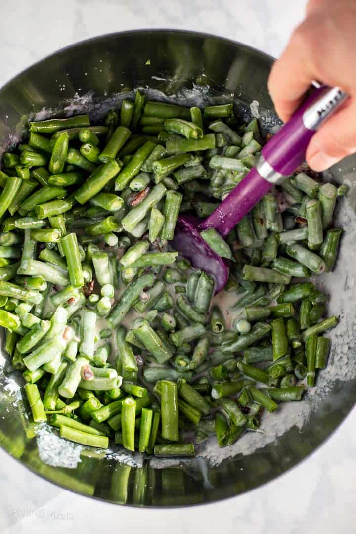 Stirring string beans and ingredients for casserole saucein a metal bowl