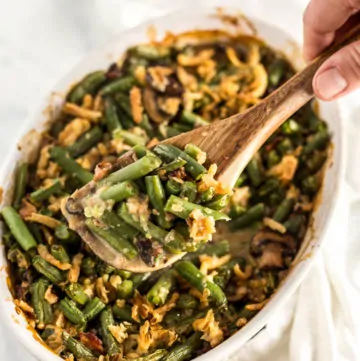 Hand scooping String Bean Casserole with Candied Bacon with a wooden serving spoon