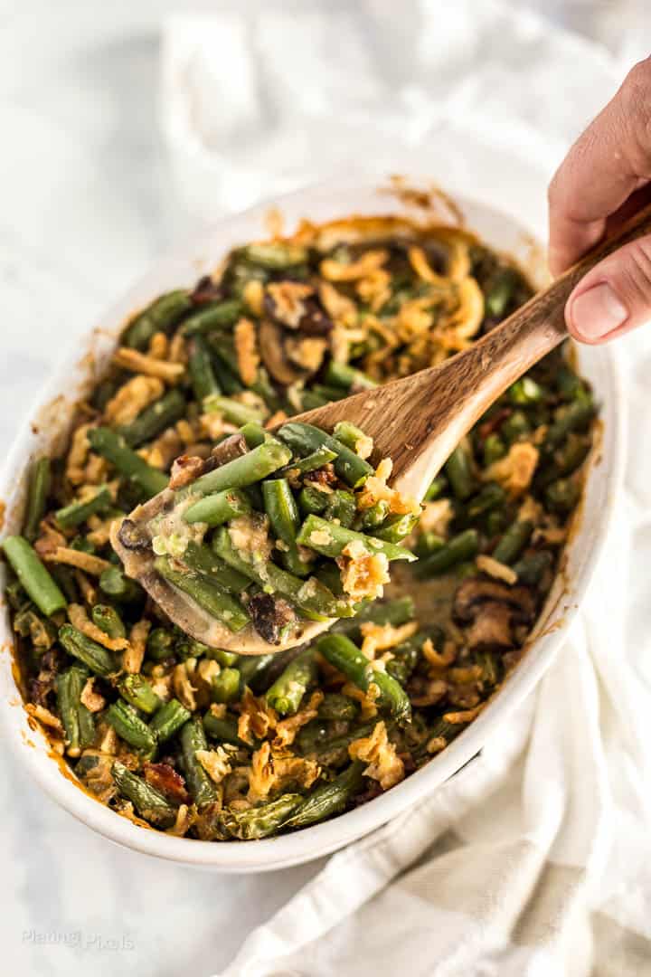 Hand scooping String Bean Casserole with Candied Bacon with a wooden serving spoon