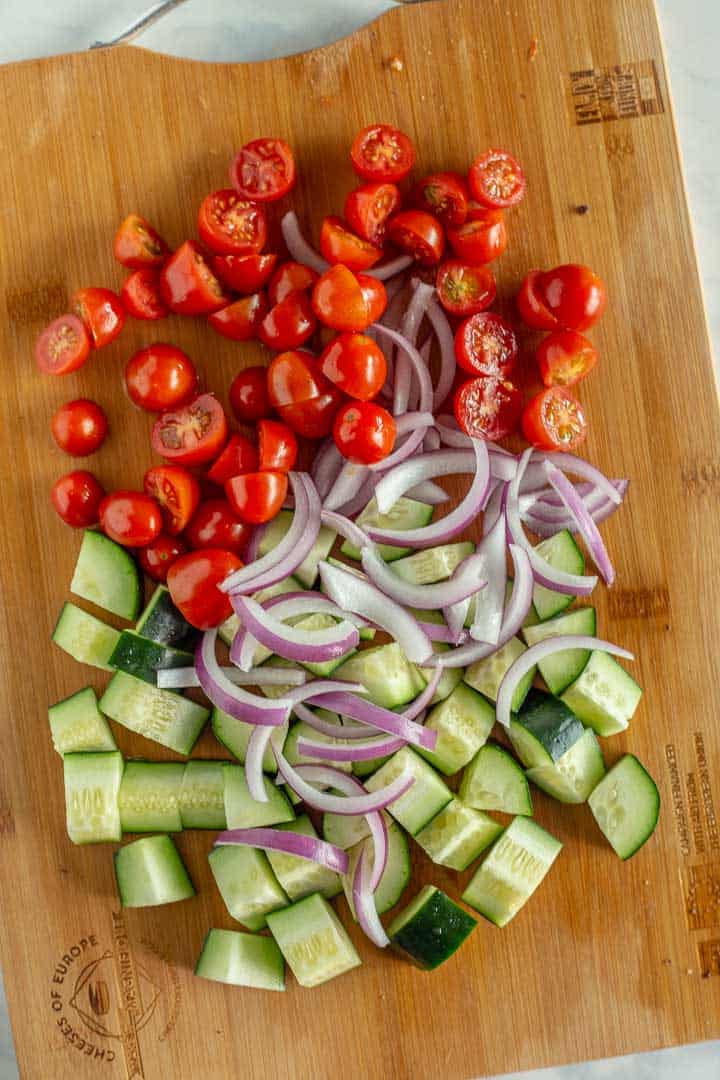 Chopped red onion, cucumber and tomatoes on a cutting board